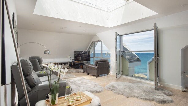 A modern living room with a large skylight, a sofa, a TV, and a view of the sea. - The Penthouse Fistral Beach -  an apartment overlooking Fistral Beach sleeping six (Newquay)