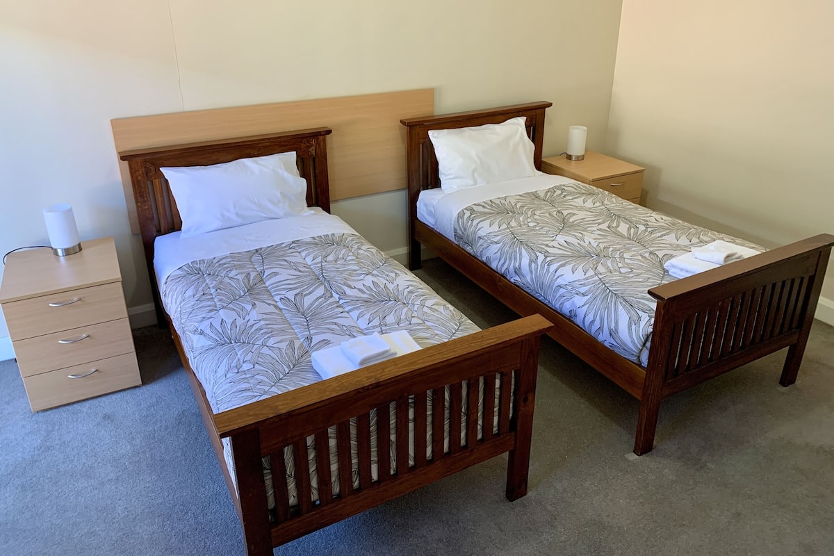 A double room with two wooden beds, each with a headboard, a bedside table, and a drawer.