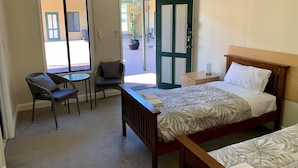Habitación de hotel con una cama, una silla, una mesita y una puerta que da al exterior.