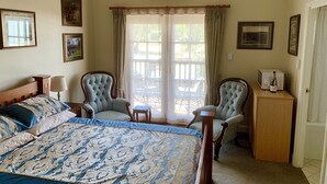 Un dormitorio con una cama grande, dos sillones, una mesita de noche de madera, un televisor y un minibar.