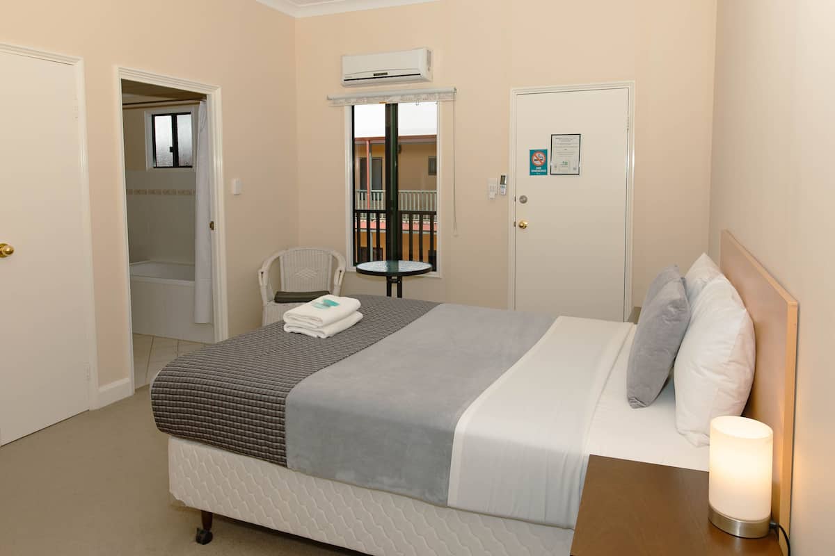 A hotel room with a bed, a chair, a table, and an air conditioning unit.