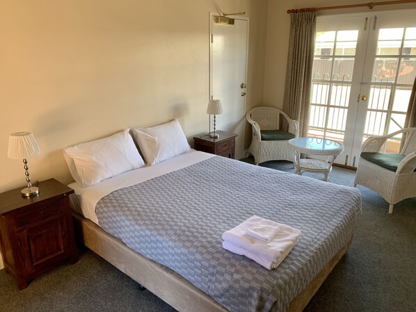 A hotel room with a large bed, a nightstand with a lamp, a chair, a small table, and a view through the window.
