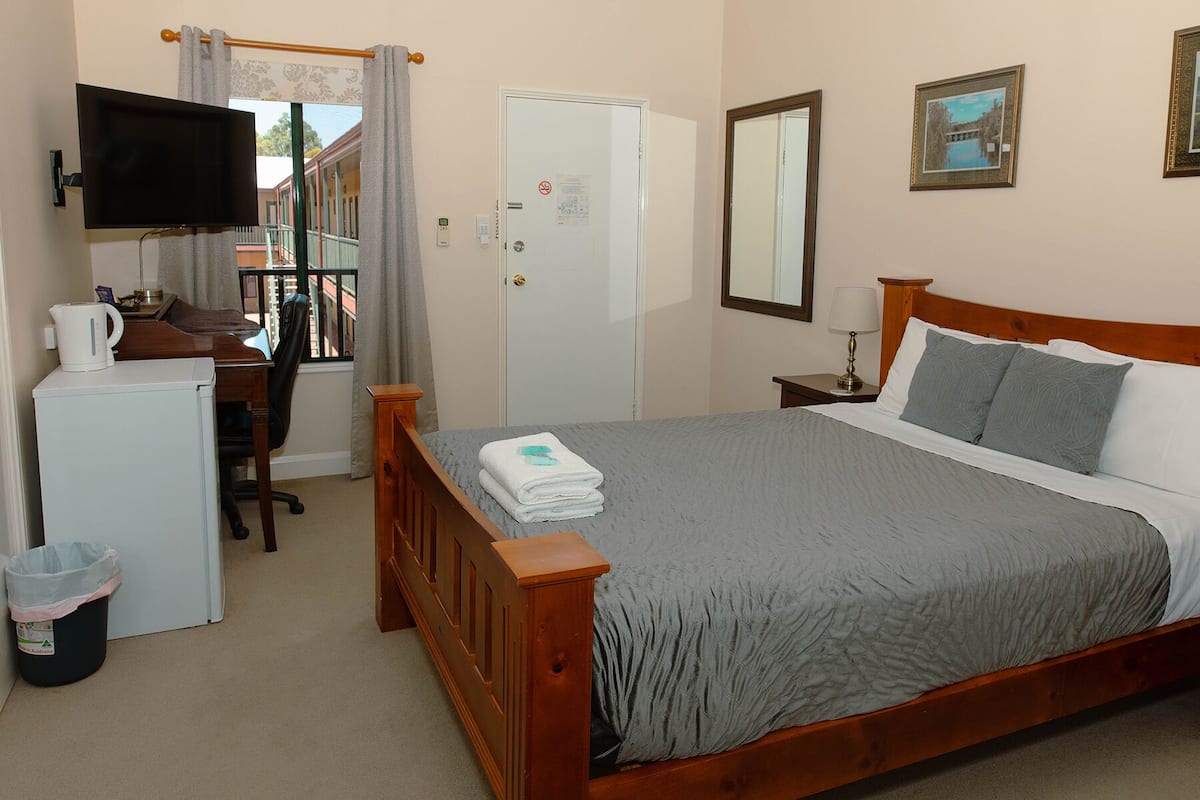 A hotel room with a bed, a desk, a television, a mirror, and a window with curtains.
