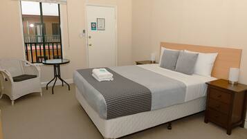 A hotel room with a bed, a chair, a small table, and a nightstand.