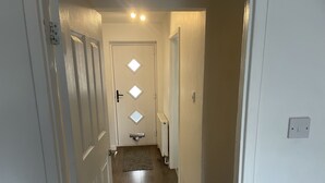 A narrow hallway with a door at the end, a light switch, and a thermostat on the wall. - 2 Bedroom River House St Neots (Saint Neots)