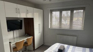 A bedroom with a bed, a desk with a chair, a TV, and a window with blinds. - 2 Bedroom River House St Neots (Saint Neots)