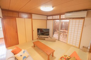 A traditional Japanese room with tatami flooring, a wooden bench, a television, sliding doors, and a wardrobe. - Dot House Naha (Naha)
