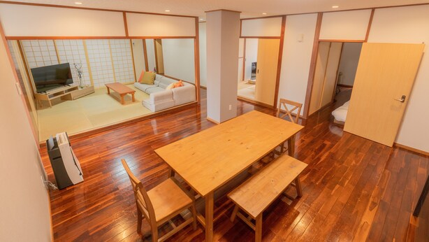 Una habitación tradicional al estilo japonés con suelo de tatami, una mesa de madera con bancos, un sofá y un televisor.