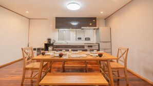 Un comedor con una mesa de madera y bancos, una cocina al fondo y una lámpara en el techo.