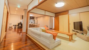 Una sala de estar moderna con un sofá, un banco, un televisor y una cocina al fondo.