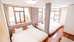 Habitación de hotel con dos camas individuales, ventanas amplias, suelo de madera y una pequeña mesa.