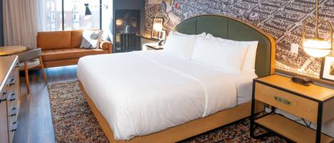 A hotel room with a large bed, a sofa, a desk, and a cityscape mural on the wall.