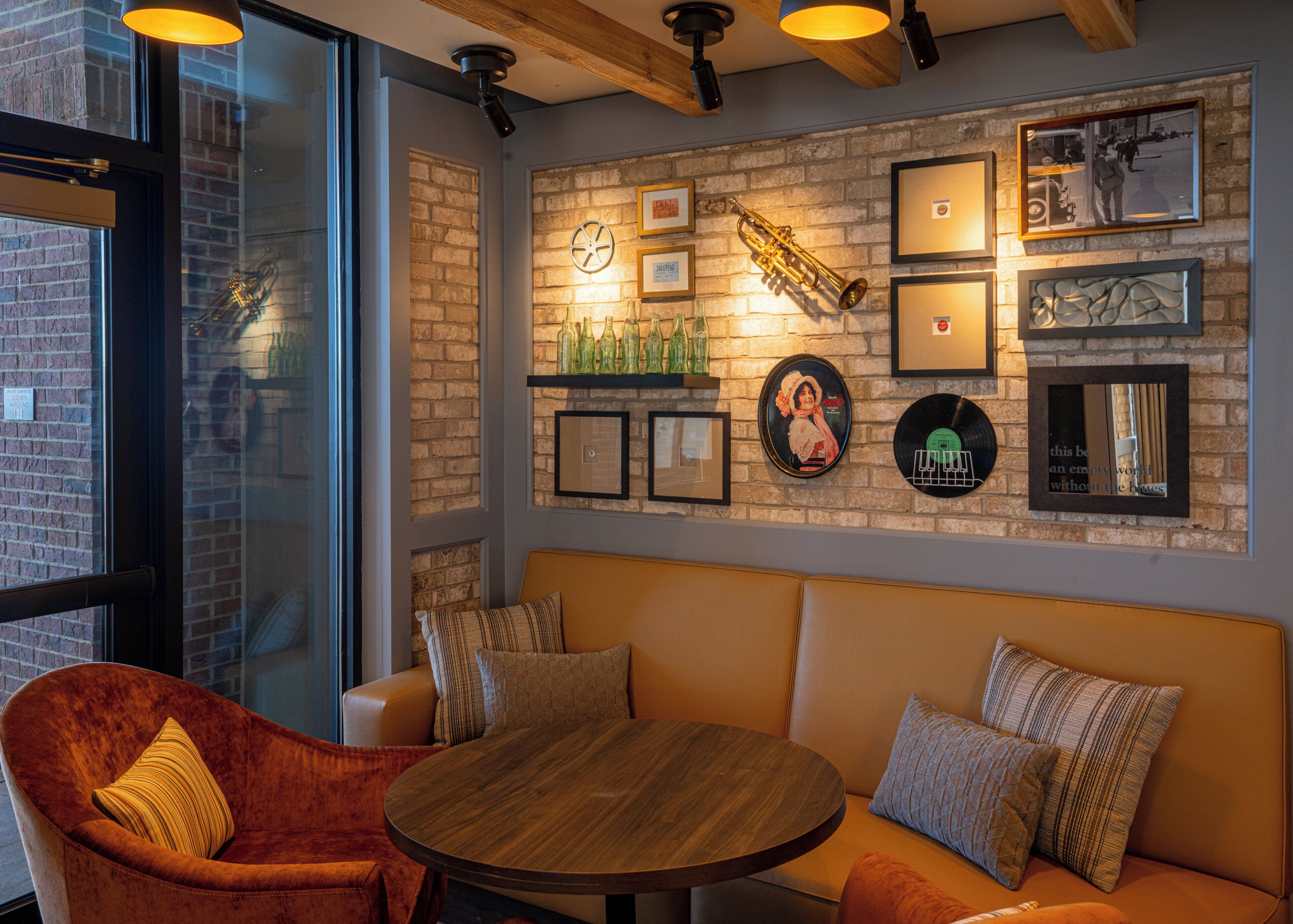 A cozy seating area with a round table, cushioned chairs, and a brick wall adorned with framed pictures and decorative items.