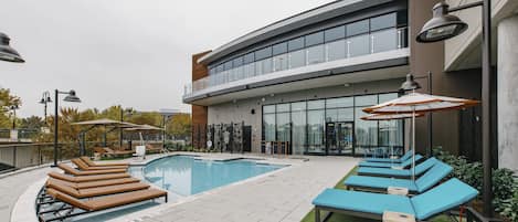 Un bâtiment moderne doté d’une piscine, de chaises longues et de parasols.