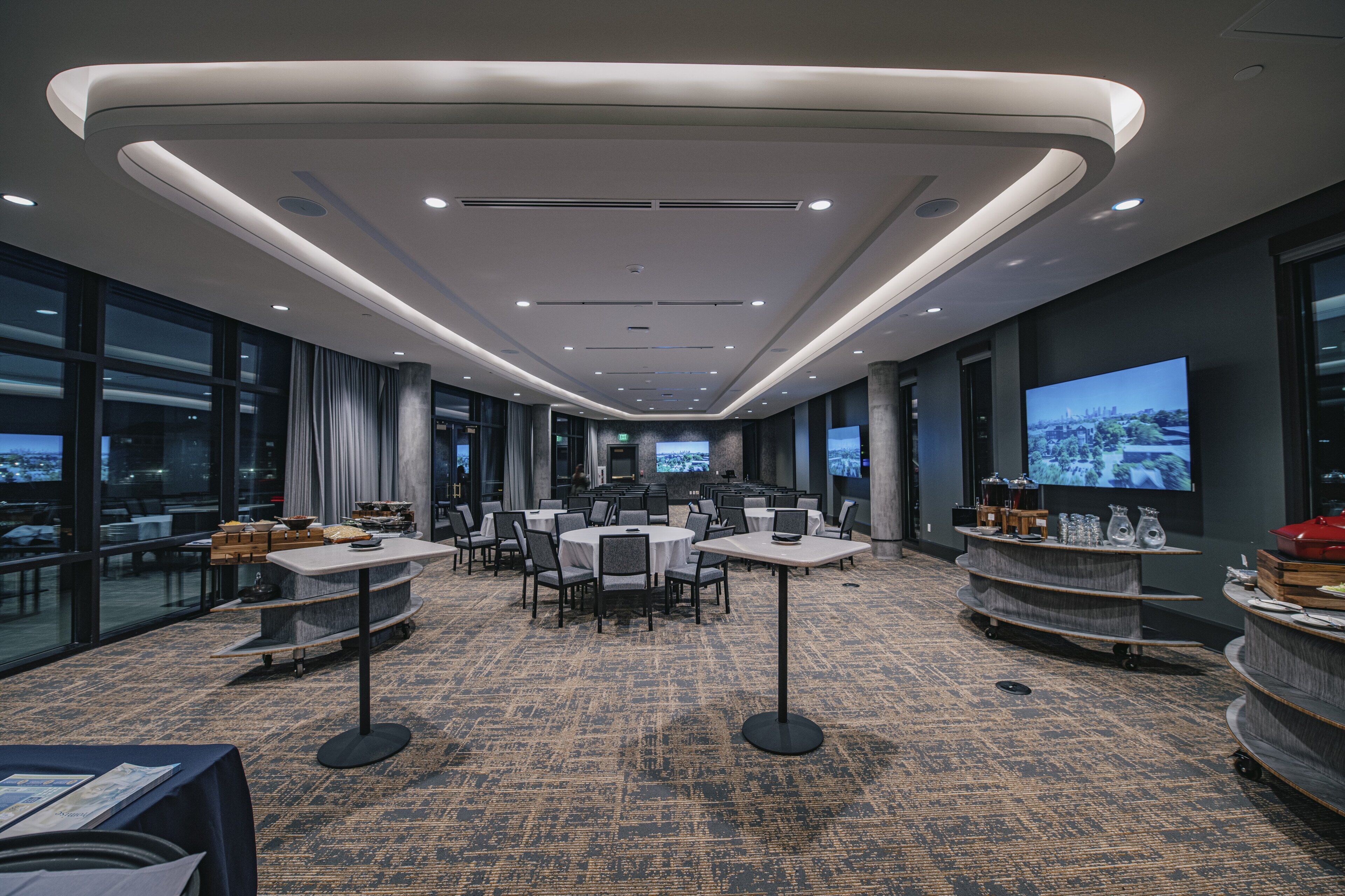 A modern conference room with round tables, chairs, a large screen, and a cityscape view.