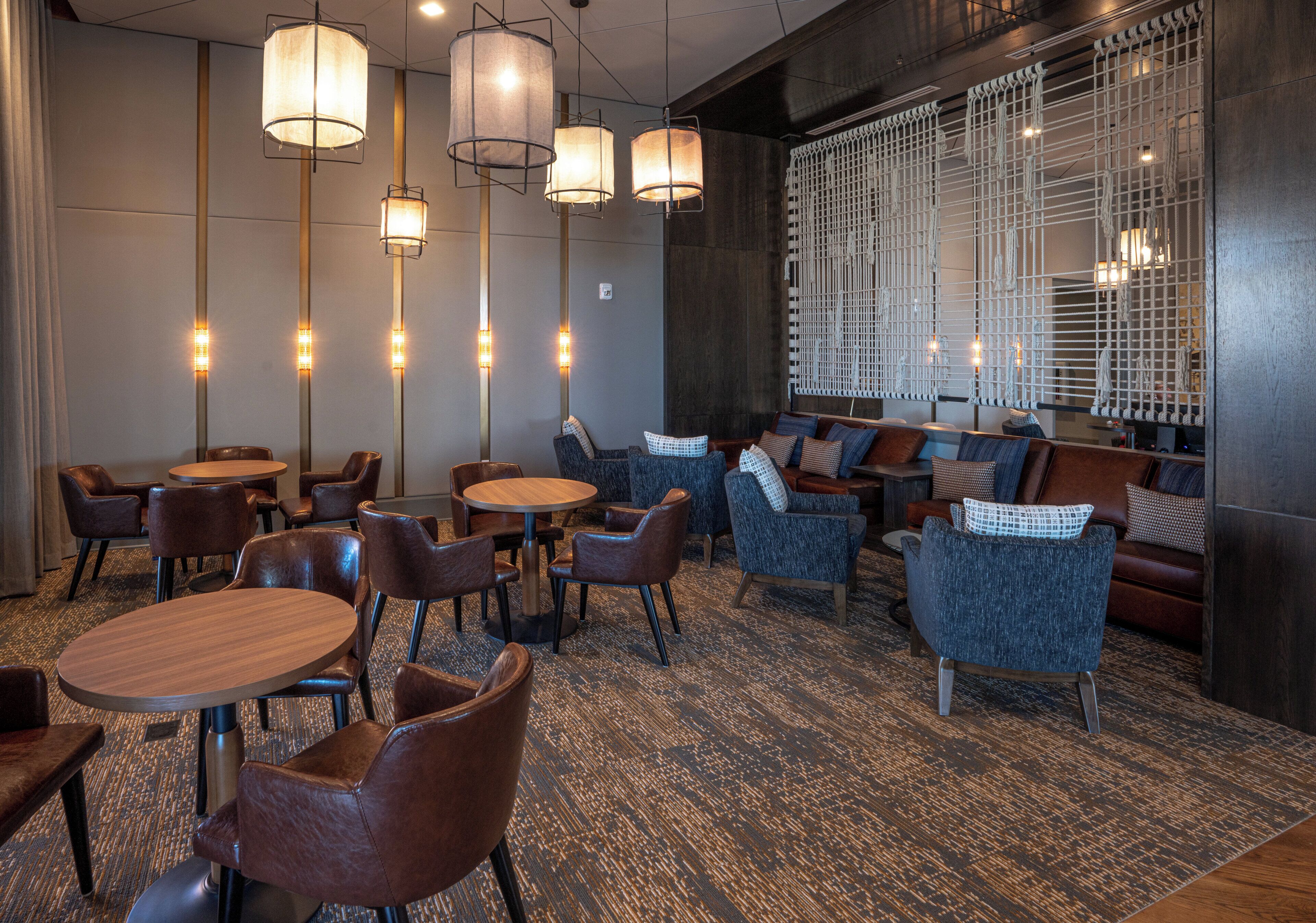 A modern interior with round tables and leather chairs, a patterned carpet, and a seating area with sofas and patterned cushions.