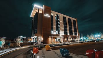 A modern hotel building with a prominent sign, a well-lit entrance, and a parking area with a distinctive sculpture.