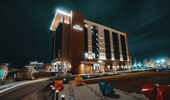 A modern hotel building with a prominent sign, a well-lit entrance, and a parking area with a distinctive sculpture.