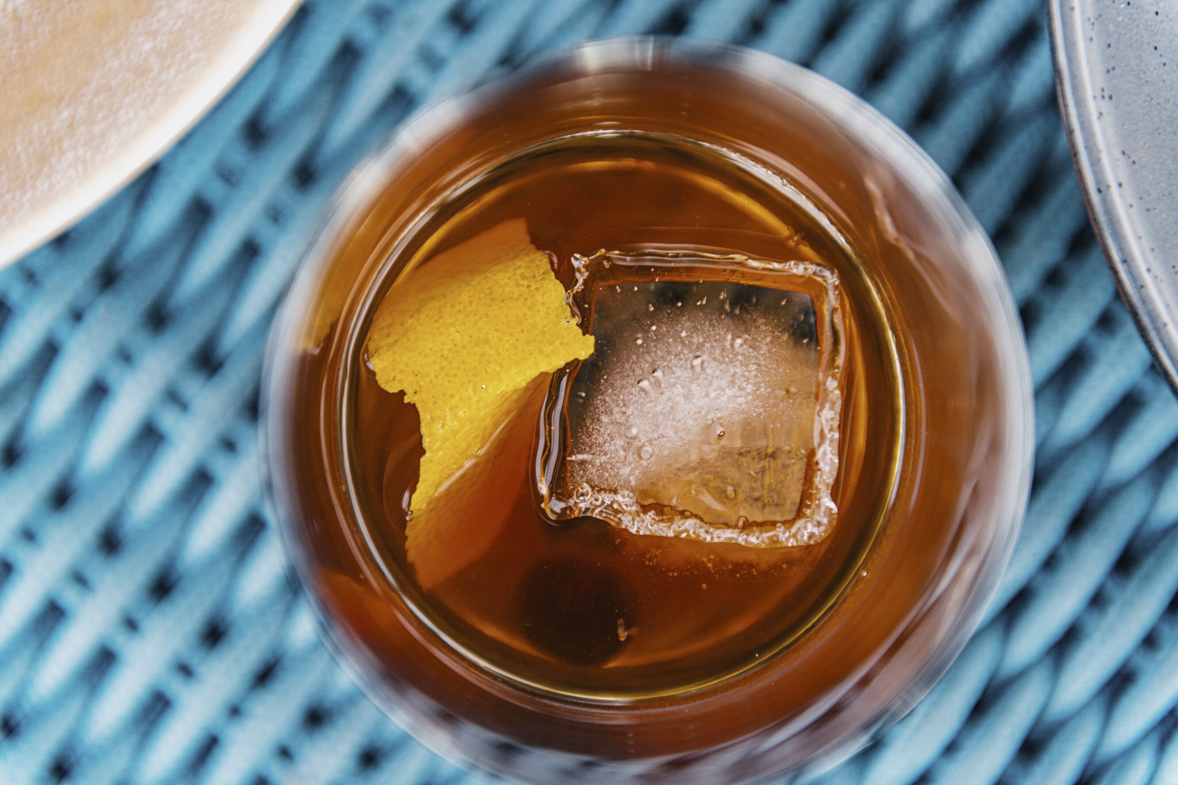 A glass of amber liquid with ice cubes and a slice of lemon.