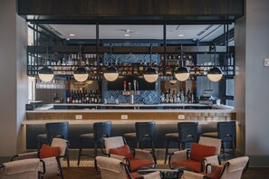 A bar area with a counter, multiple chairs, and a variety of bottles and glasses on shelves. - Hotel Indigo Columbus at Riverfront Place by IHG (Columbus)