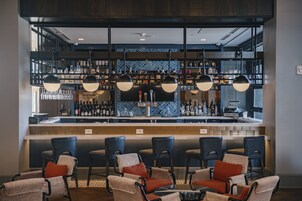 A bar area with a counter, multiple chairs, and a variety of bottles and glasses on shelves.