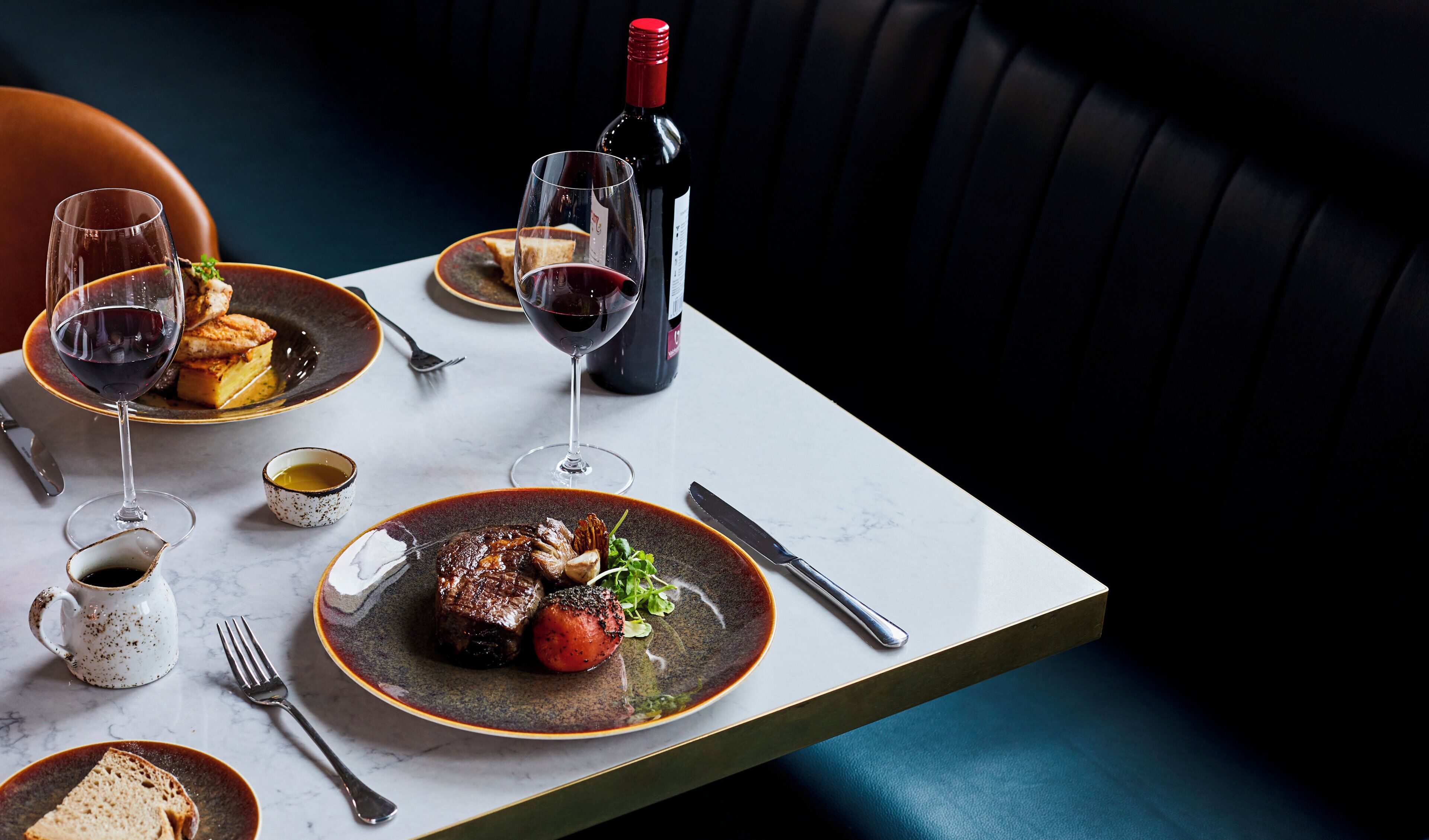 A dining table with plates of food, wine glasses, and a bottle of wine.
