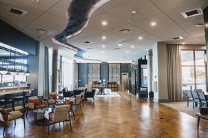 En rymlig hotellobby med modern design, som inkluderar en bardel, sittgrupper och stora fönster som släpper in naturligt ljus.