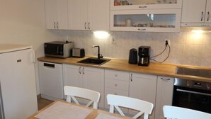 Una cucina compatta con mobili bianchi, un forno a microonde, un tostapane, una macchina da caffè e un frigorifero.