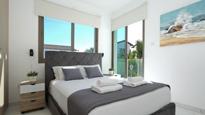 A modern bedroom with a large bed, a nightstand, a potted plant, and a view of the outdoors. - VILLA APOLLONIA - Brand new villa walking to Trinity Beach (Paralimni)
