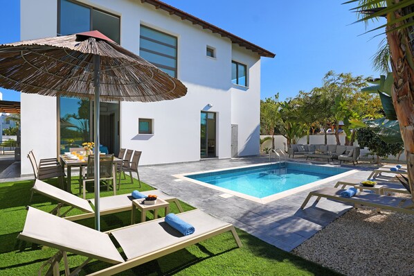 A modern house with a swimming pool, outdoor seating, and a well-maintained lawn. - VILLA APOLLONIA - Brand new villa walking to Trinity Beach (Paralimni)