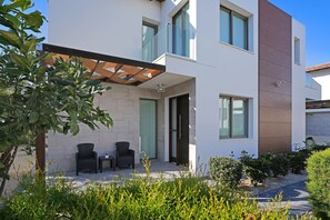A modern two-story house with a covered patio, outdoor seating, and a well-maintained garden. - VILLA APOLLONIA - Brand new villa walking to Trinity Beach (Paralimni)