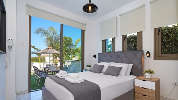 A modern bedroom with a large bed, a bedside table, and a view of the outdoors. - VILLA APOLLONIA - Brand new villa walking to Trinity Beach (Paralimni)