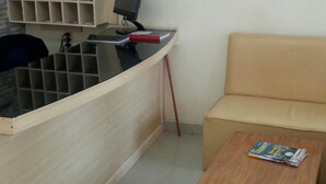 Ein Zimmer mit einem Holztisch, einem Computer, einem beigen Sofa und einem kleinen Holztisch mit Zeitschriften.