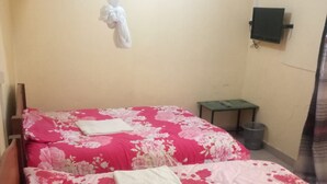 Ein Zimmer mit zwei Betten, jeweils mit einer rosa Blumenüberwurf und weißen Kissen. In der Ecke befindet sich ein kleiner Tisch und ein Mülleimer.