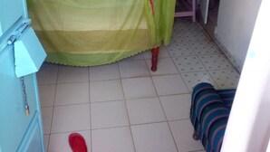 Ein Zimmer mit einem Bett, das von einem grünen Baldachin bedeckt wird, einem kleinen Holzschemel und einer gestreiften Decke auf dem Boden.