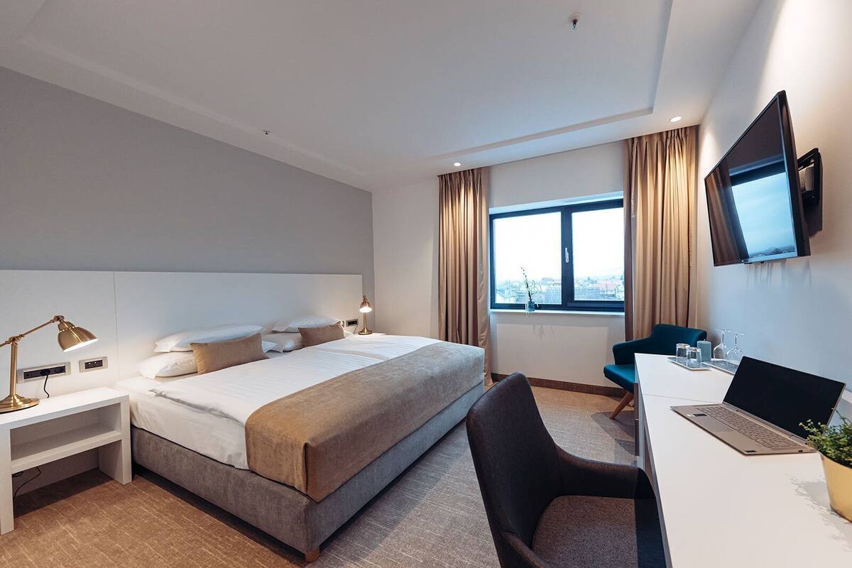 Une chambre d’hôtel équipée d’un lit, d’un bureau, d’une chaise, d’une télévision et d’une fenêtre avec des rideaux.