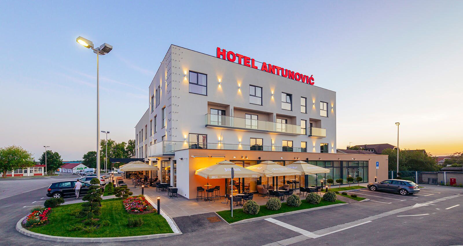 Un hôtel moderne doté d’un toit plat, de nombreuses fenêtres et d’un espace extérieur aménagé avec des parasols.