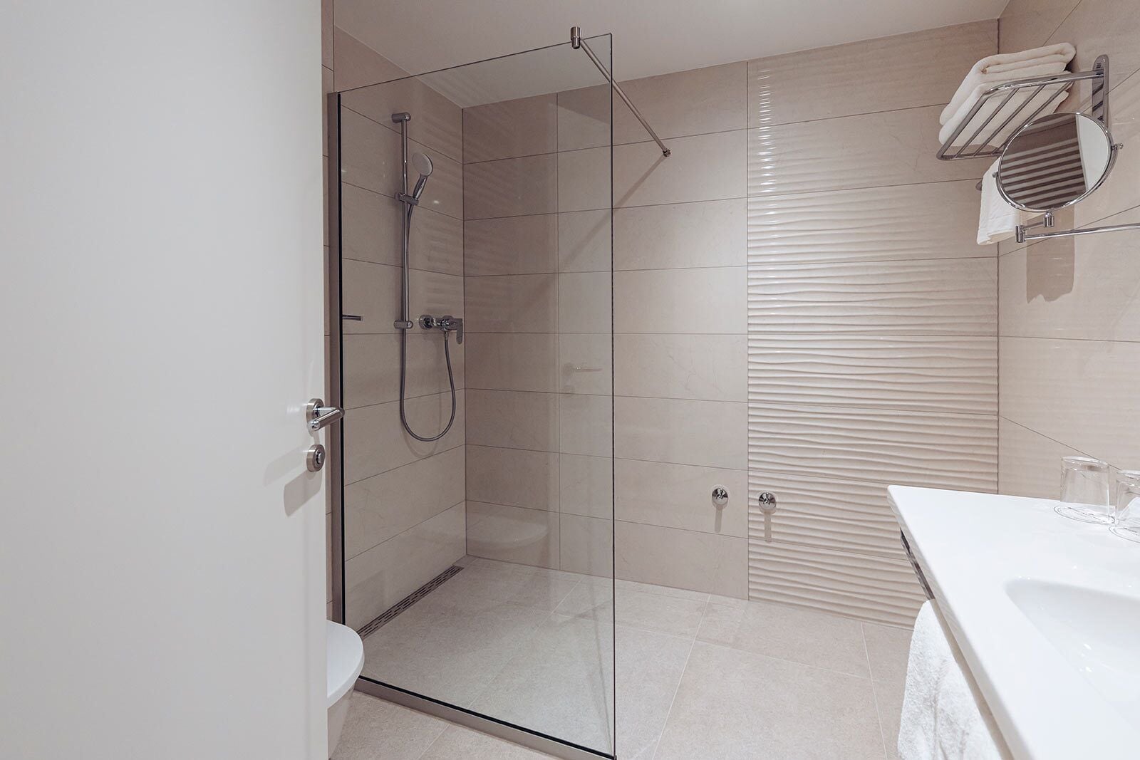 Un baño moderno con ducha de vidrio, lavamanos blanco y perchero para toallas.
