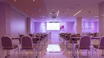 A conference room with rows of chairs, a large screen at the front, and a modern ceiling design.