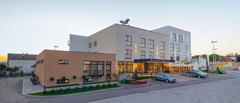 Un hotel moderno con estructura de dos pisos, entrada cubierta y estacionamiento con varios coches.