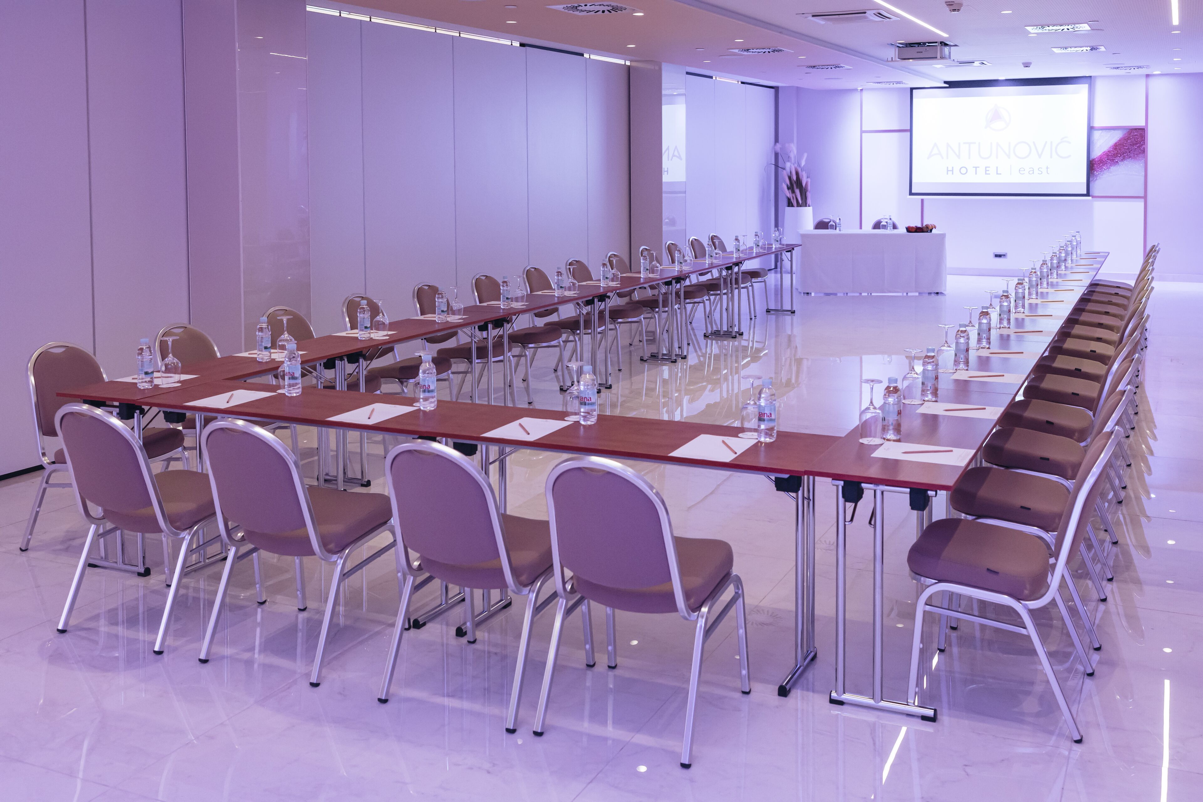 Ein Konferenzraum mit einem langen Tisch, Stühlen und einem Bildschirm, der den Namen des Hotels zeigt.