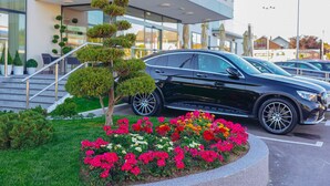 Een modern hotel met een trap naar de ingang, een zwarte auto ervoor geparkeerd en een bloembed met verschillende bloemen.