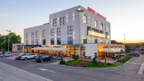 Een modern hotel met een opvallend bord met de tekst 'HOTEL ANTUNOVIC', een terras en een parkeerplaats.