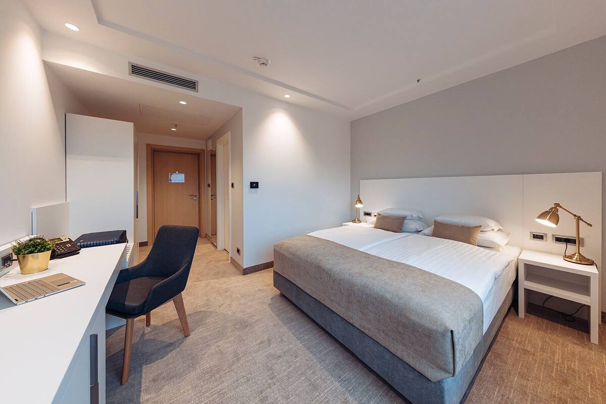 Une chambre d’hôtel moderne avec un grand lit, un bureau avec un ordinateur portable, une chaise et des lampes de chevet.