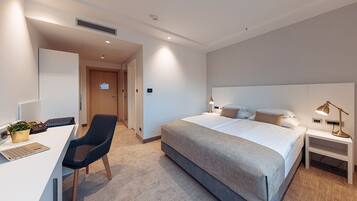 A modern hotel room with a large bed, a desk with a laptop, a chair, and bedside lamps.
