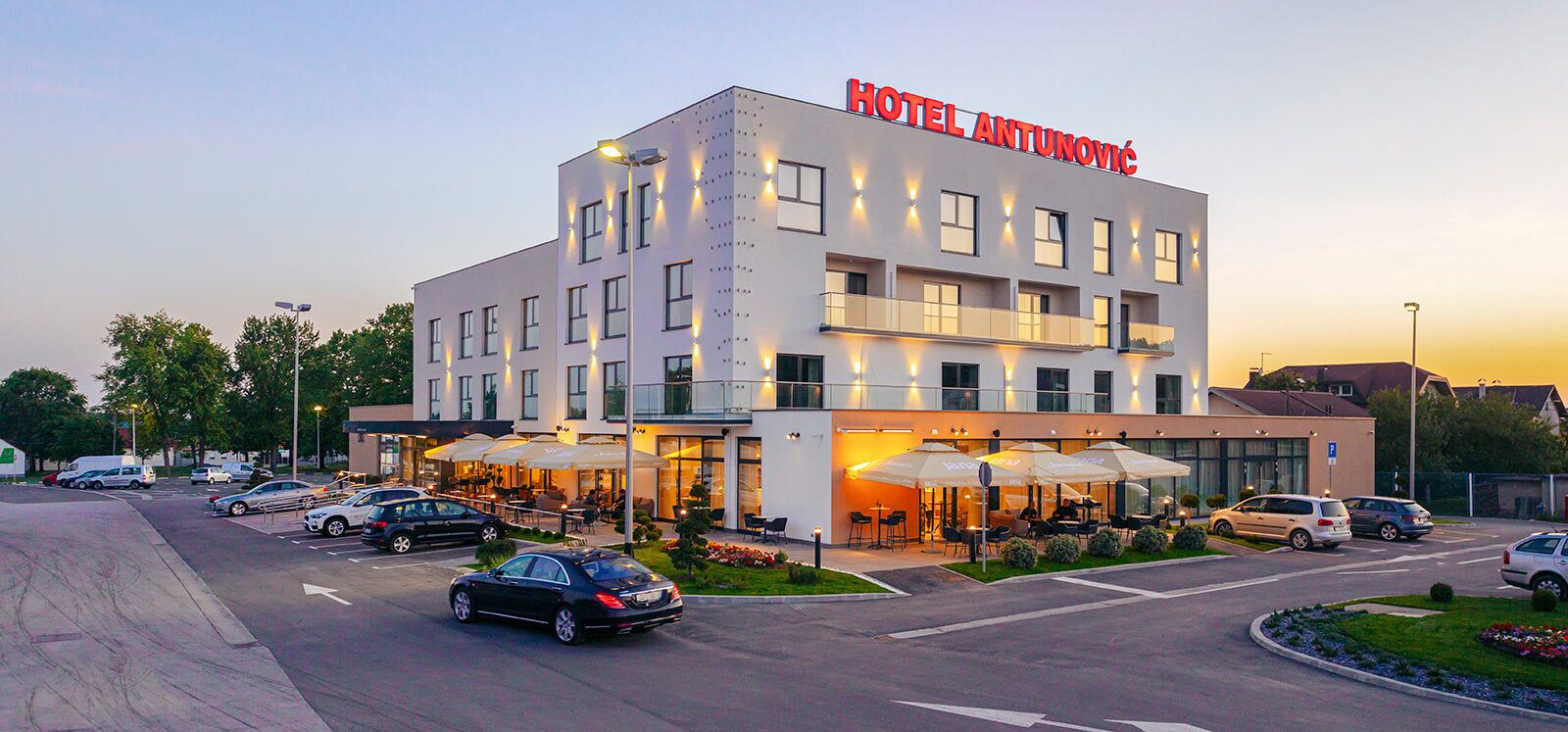 A modern hotel with a prominent sign, multiple floors, outdoor seating, and a parking area.