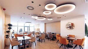 Een moderne eetruimte met ronde tafels en oranje stoelen, met plafondlampen en een groot raam op de achtergrond.