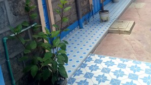 A building with a tiled porch, a blue door, and potted plants. - Bidii Bar & Restaurant (Mai Mahiu)