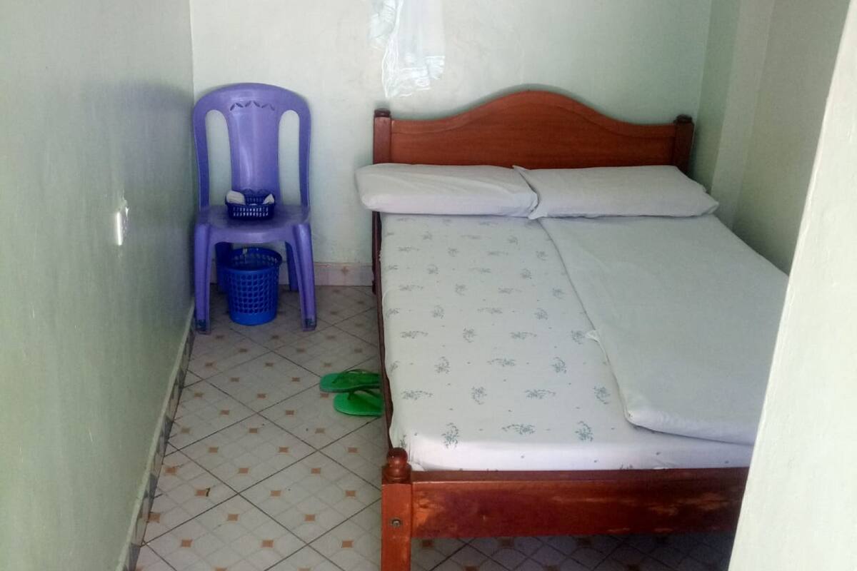 A small room with a wooden bed, a purple chair, and a blue basket on the floor.