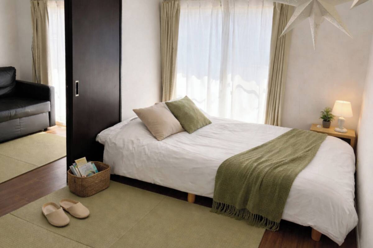 A bedroom with a bed, a bedside table with a lamp, a chair, and a basket on the floor.